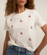 Remera t-shirt blanca de algodón con cuello redondo y mangas cortas. Presenta bordados de cerezas rojas dispersos en el frente.