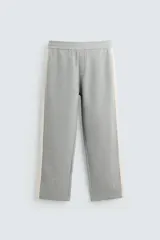 Pantalón de jogging gris con corte relaxed fit, cintura elástica ajustable con cordón interior, bolsillos laterales y traseros de vivo, y banda lateral color crema.