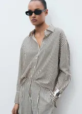 Camisa oversize a rayas verticales negras y beige, con cuello camisero, cierre frontal con botones y mangas largas abotonadas.