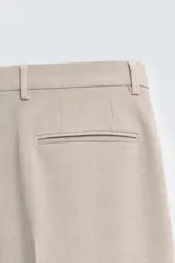 Pantalón de vestir color beige, corte slim fit, con bolsillos laterales y traseros con doble vivo y botón. Cierre frontal con cremallera y botón.