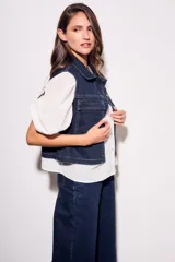 Chaleco de jean azul oscuro con cuello, bolsillos frontales y cierre con botones dorados. Corte al cuerpo.