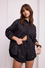 Camisa negra con bordado de flores rosas, corte recto, cuello clásico y cierre frontal con botones.