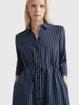 Vestido camisero midi azul marino con rayas verticales blancas, cuello camisero, cierre frontal con botones, mangas largas con puños abotonados y cinturón de lazo a juego.