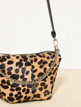 Bandolera confeccionada en cuero con estampado animal print, detalles en cuero vacuno y cadena metálica plateada en el frente. Tiene correa regulable de cuero y bolsillo interno con cierre.