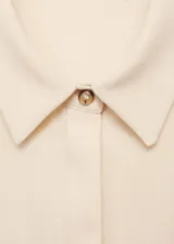 Vestido color crema de tejido fluido, con cuello camisero, mangas cortas con vuelta, detalles drapeados, diseño midi y entallado, y cierre delantero de botones oculto.