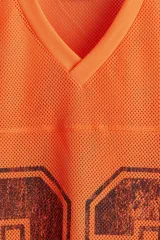 Remera de malla color naranja vibrante, estilo jersey de fútbol americano, con cuello en V y corte oversized. Presenta un estampado grande y desgastado del número "22" en color negro o marrón oscuro en el frente.