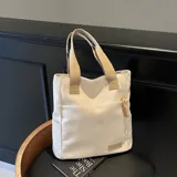 Bolso tipo tote color crema, con doble asa corta y tira larga regulable en color beige. Tiene un bolsillo externo con cierre y un parche con el logo de la marca.