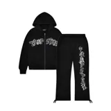 Conjunto deportivo negro de buzo con capucha y pantalón de jogging, ambos con logo "Trapstar" en letras góticas blancas con contorno plateado. El buzo tiene cierre frontal y bolsillo tipo canguro. El pantalón tiene cordón ajustable en la cintura y tobillos ajustables.