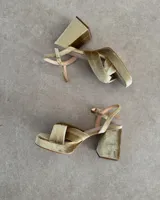 Sandalia de cuero vacuno color dorado, con plataforma y taco cuadrado. Presenta una tira delgada en el tobillo y detalle de nudo en la capellada.