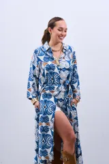 Vestido estilo camisola con estampado floral en tonos azules y marrones, con cuello camisero, mangas largas con puños y cierre frontal con botones. Incluye cinturón de la misma tela.
