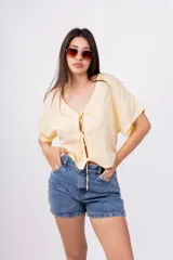 Remera color amarillo pálido de corte holgado, escote en V con lazo y mangas cortas.