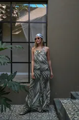 Mono largo de mujer, color verde oliva con estampado de hojas de palmera en blanco. Diseño de tirantes finos y escote en V con detalle de adorno tipo concha o broche en el centro del busto. El calce es holgado y fluido.