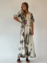 Vestido largo color beige con estampado tie-dye en tonos rosados, corte amplio, mangas cortas con volados y ruedo con flecos.
