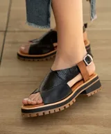 Sandalia de cuero vacuno color negro con detalles en marrón, suela de goma deportiva, hebilla a la altura del tobillo y horma ancha.