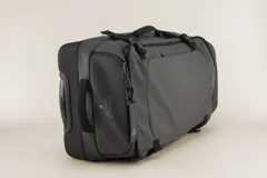 Valija gris con ruedas, manija extensible y correas de ajuste externas.