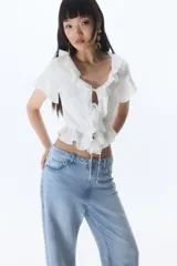 Blusa blanca entallada corta en tejido liviano de mezcla de lino y viscosa. Modelo de manga corta con escote redondo pronunciado, delantero abierto con tira fina doble y cordón para ajustar en la cintura. Volados anchos en escote, abertura, mangas y bajo.