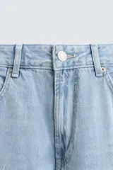 Pantalón de jean celeste de corte flare, con tiro medio, cinco bolsillos, cierre frontal con cremallera y botón, y bajo con acabado irregular.