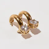 Aros tipo argolla dorados con un cristal redondo colgando.