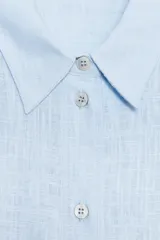 Camisa amplia color negro confeccionada con hilatura de lino. Tiene cuello solapa, manga larga, bolsillo de plastrón en el delantero, bajo asimétrico y cierre frontal con botones.