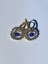 Aros dorados con dije circular de resina y strass, con flor de vidrio verde en el interior. El arito es de acero quirúrgico.