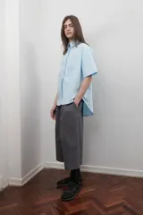 Bermuda gris unisex de corte amplio, con pretina elástica, tiro bajo, bolsillos laterales y cierre lateral. Presenta un pliegue delantero de gran tamaño.