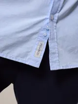 Camisa de manga larga con estampado a cuadros azul y blanco, confeccionada en algodón con efecto peach y bolsillo en el pecho.