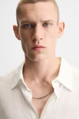 Camisa de hombre color blanco, de manga larga y cuello solapa, con un patrón jacquard sutil a cuadros. Presenta un calce relajado (relaxed fit) y bajo con aberturas laterales.