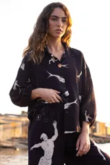 Camisa negra con estampado de sirenas blancas, cuello clásico, cierre con botones y mangas 3/4 abullonadas con lazos en los puños.