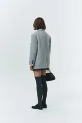 Blazer de lana con mezcla de alpaca en color gris claro, con cuello sastre, cierre frontal de dos botones y bolsillos laterales con solapa. Presenta una textura suave y ligeramente vellosa que aporta calidez.