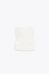 Top bustier blanco con escote corazón y hombros descubiertos. Detalle de tapetas delanteras combinadas con tejido satinado a tono. Cierre frontal con botones.