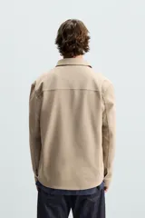 Sobrecamisa negra de tejido con elasticidad, cuello solapa, manga larga con puño abotonado, bolsillos de plastrón en el pecho y cierre frontal con botones a presión.