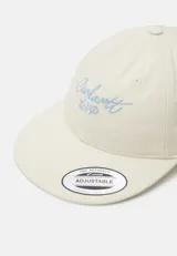 Gorra de béisbol color crema con logo Carhartt WIP bordado en celeste en el frente. Tiene visera curva y correa ajustable en la parte trasera.