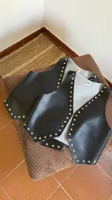 Chaleco negro de ecocuero con tachas doradas.