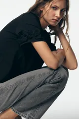 Camiseta negra de algodón con cuello redondo, manga corta y detalle de flores con volumen en las mangas.