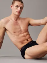 Pack de tres slips negros de algodón con cintura elástica con logo de Calvin Klein en blanco y rojo.