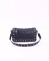 Bandolera negra de cuero con tachas plateadas. Tiene dos asas desmontables: una corta con tachas para llevarla en la mano o al hombro, y una larga para llevarla al hombro o cruzada.