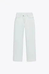 Jeans tobilleros de tiro alto color blanco, corte recto y bajo sin costura. Cierre frontal cruzado con cremallera y botones.
