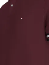 Chomba Tommy Hilfiger color borgoña de corte regular, confeccionada en algodón orgánico y elastano. Presenta cuello tipo polo con cartera de dos botones, detalles distintivos de la marca y logo bordado en el pecho.