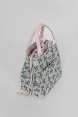 Lunchera térmica de tela color gris claro con estampado de hojas verdes y asas de tela color crudo. Tiene un bolsillo externo con cierre de botón a presión y cierre superior con cordón ajustable.
