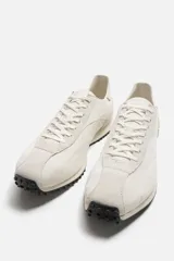 Zapatillas deportivas color crema con cordones, estilo retro. Parte superior fabricada en tejido técnico y detalles en piel con acabado serraje. Suela dentada con detalle a contraste en negro.