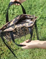 Cartera tipo tote de cuero color blanco con manchas doradas, doble asa corta y flecos de cuero en los laterales.