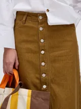 Falda midi de denim color marrón con hilado a la vista en el ruedo y abotonadura frontal.