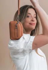 Monedero negro de simil cuero con correa para la mano, diseño práctico y compacto. Bolsillo principal con doble cierre, y un bolsillo frontal pequeño para llevar monedas.