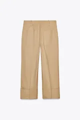 Pantalón color beige de corte ancho, con tiro medio, trabillas en la cintura y raya planchada.