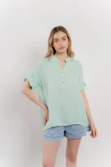 Blusa color verde agua confeccionada en lino, de corte recto, escote en V abotonado y mangas cortas arremangables.