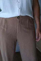 Pantalón de vestir de tiro alto, color tostado con finas rayas verticales blancas. Presenta un corte ancho y fluido, con pinzas frontales y cierre de botón.