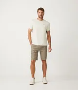 Bermuda masculina color caqui, corte slim, confeccionada en sarga lisa de algodón y elastano, con bolsillos laterales y cierre con botón y cremallera.