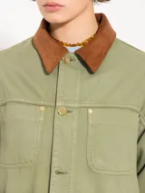 Chaqueta verde militar de algodón con cuello marrón de pana, cierre frontal con botones dorados, bolsillos plaqué en la parte superior e inferior y corte holgado.