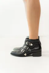 Botas cortas de cuero negro con puntera fina, taco bajo y cierre lateral. Presentan tres correas con hebillas plateadas y apliques de tachas plateadas.