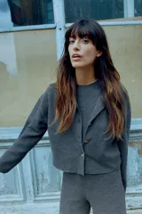 Chaqueta color crema de punto canalé con cuello redondo, manga larga y cierre frontal con botones marrones.